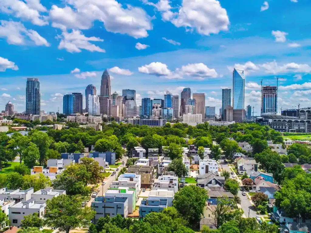 Aerial daytime view of the Charlotte, NC skyline behind a tree lined neighborhood