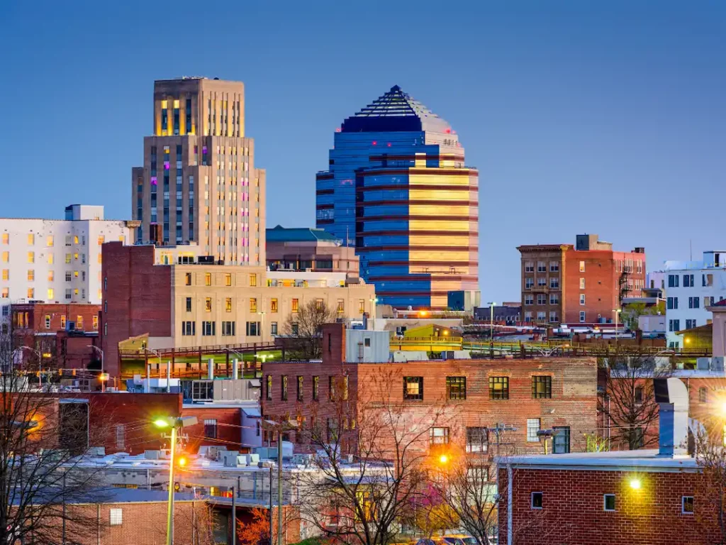 Aerial view of a historic Durham, NC mill district with a brick smokestack and water tower at sunset