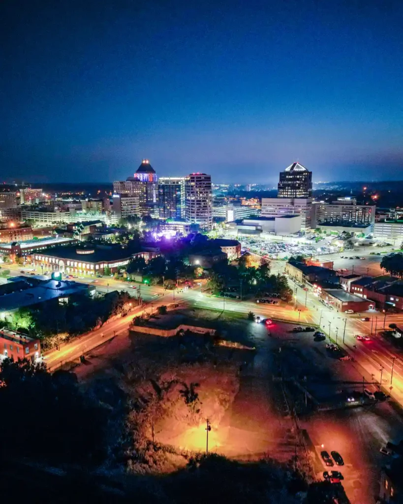 Aerial dusk view of downtown Greensboro, NC with an illuminated park and city skyline