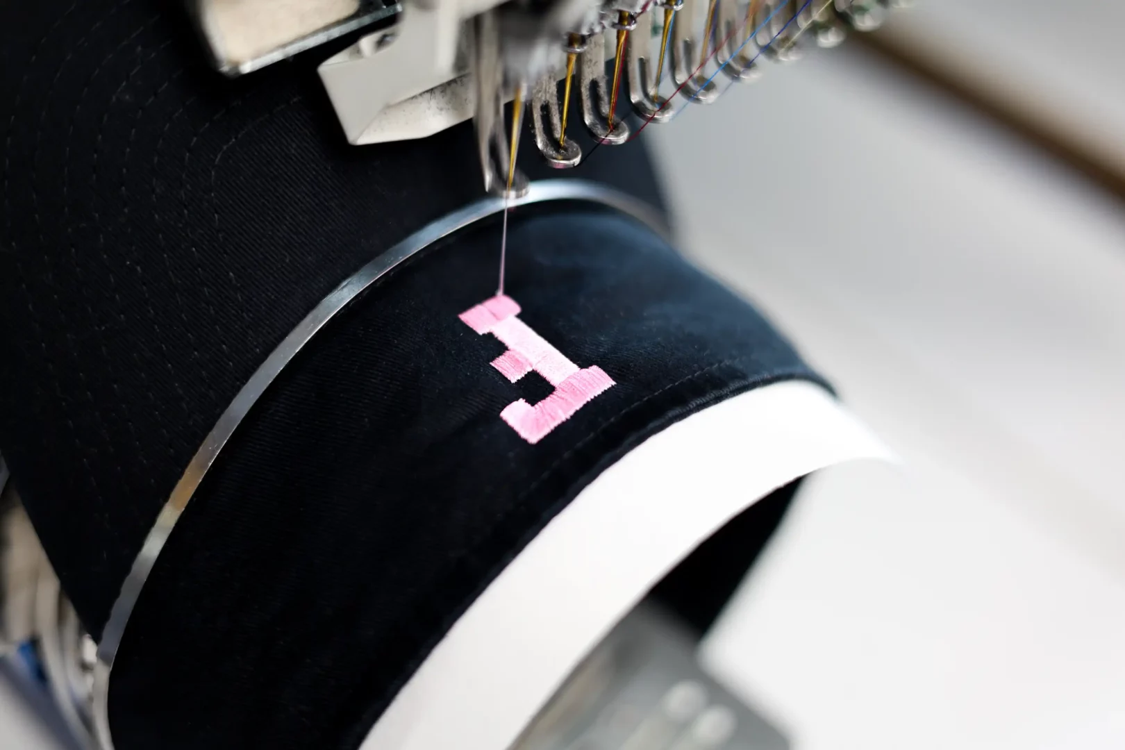 Close-up of a pink letter being embroidered onto a custom visor
