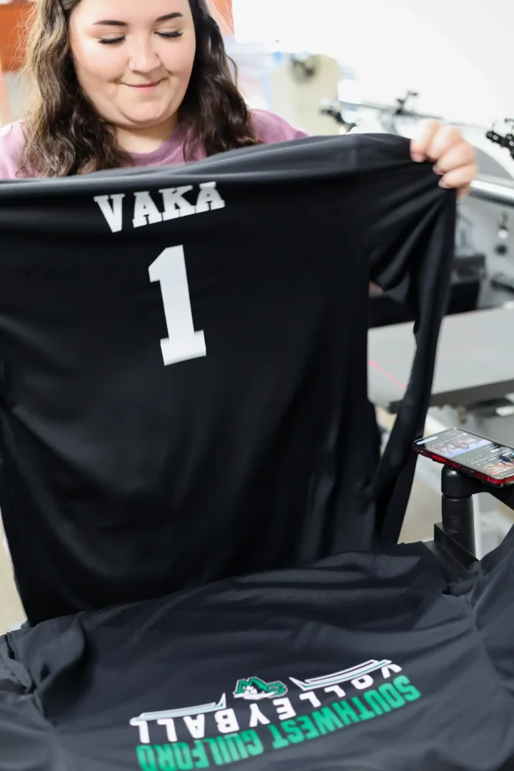 Employee reviewing finished custom volleyball jerseys with name and number transfers